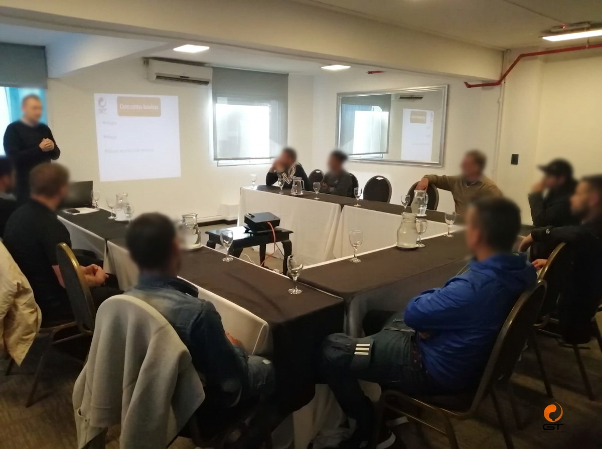 Formación en sala con mesas dispuestas para un grupo y rostros difuminados
