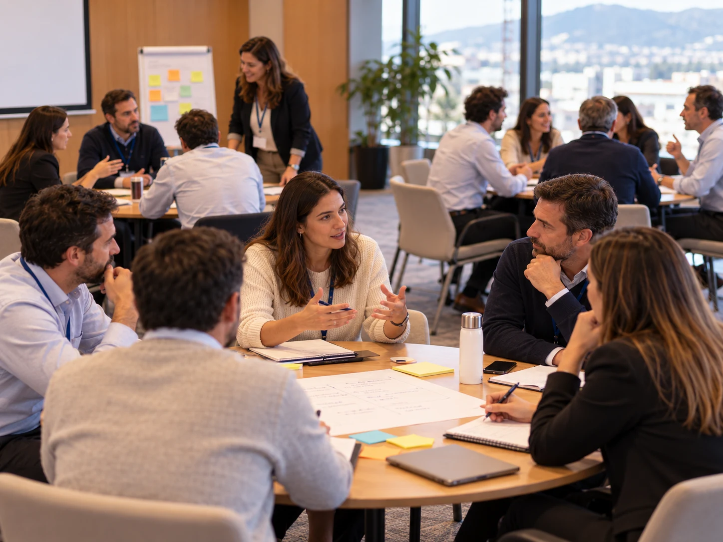 Ilustración conceptual de un taller de liderazgo con profesionales trabajando en equipos alrededor de mesas y una facilitadora acompañando la actividad