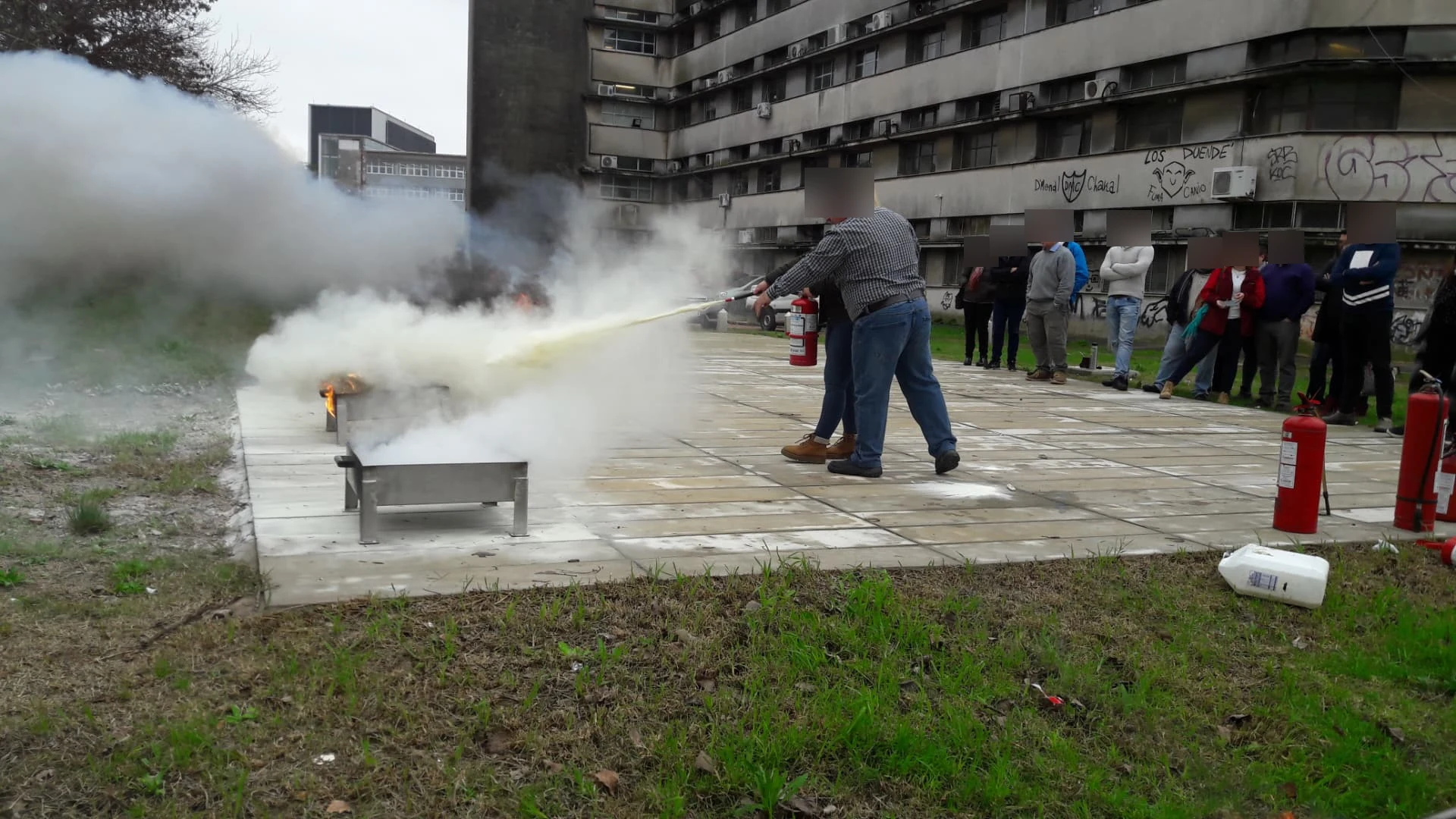 Práctica supervisada con un extintor portátil sobre fuego controlado y participantes observando