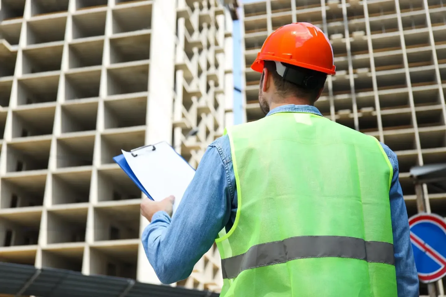 Profesional con casco naranja y chaleco reflectante revisando una planilla frente a una estructura en construcción